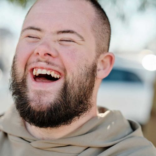 A headshot of a man with Down Syndrome laughing heartily. Shot with a blurred background.